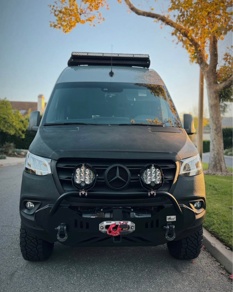 This custom Mercedes Sprinter off-road RV rental boasts a robust front bumper, winch, and roof light bar, parked under autumn leaves. — photo 7