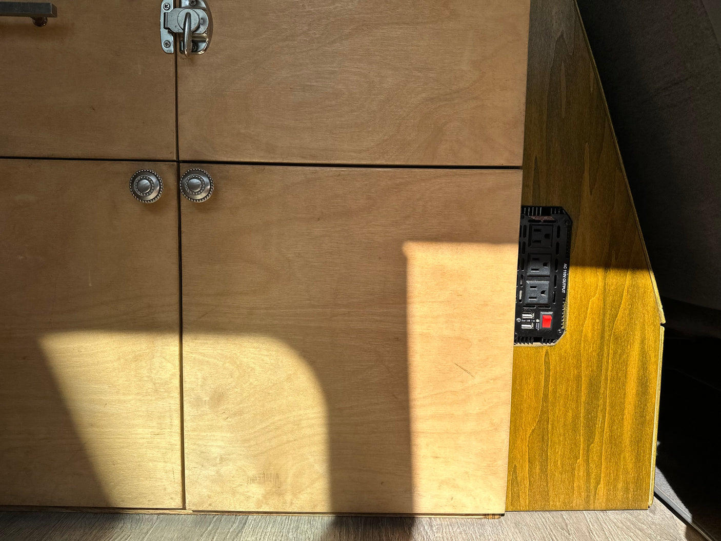 RV rental interior with custom wooden cabinets, power inverter (AC/USB outlets). Sunlight streams in.