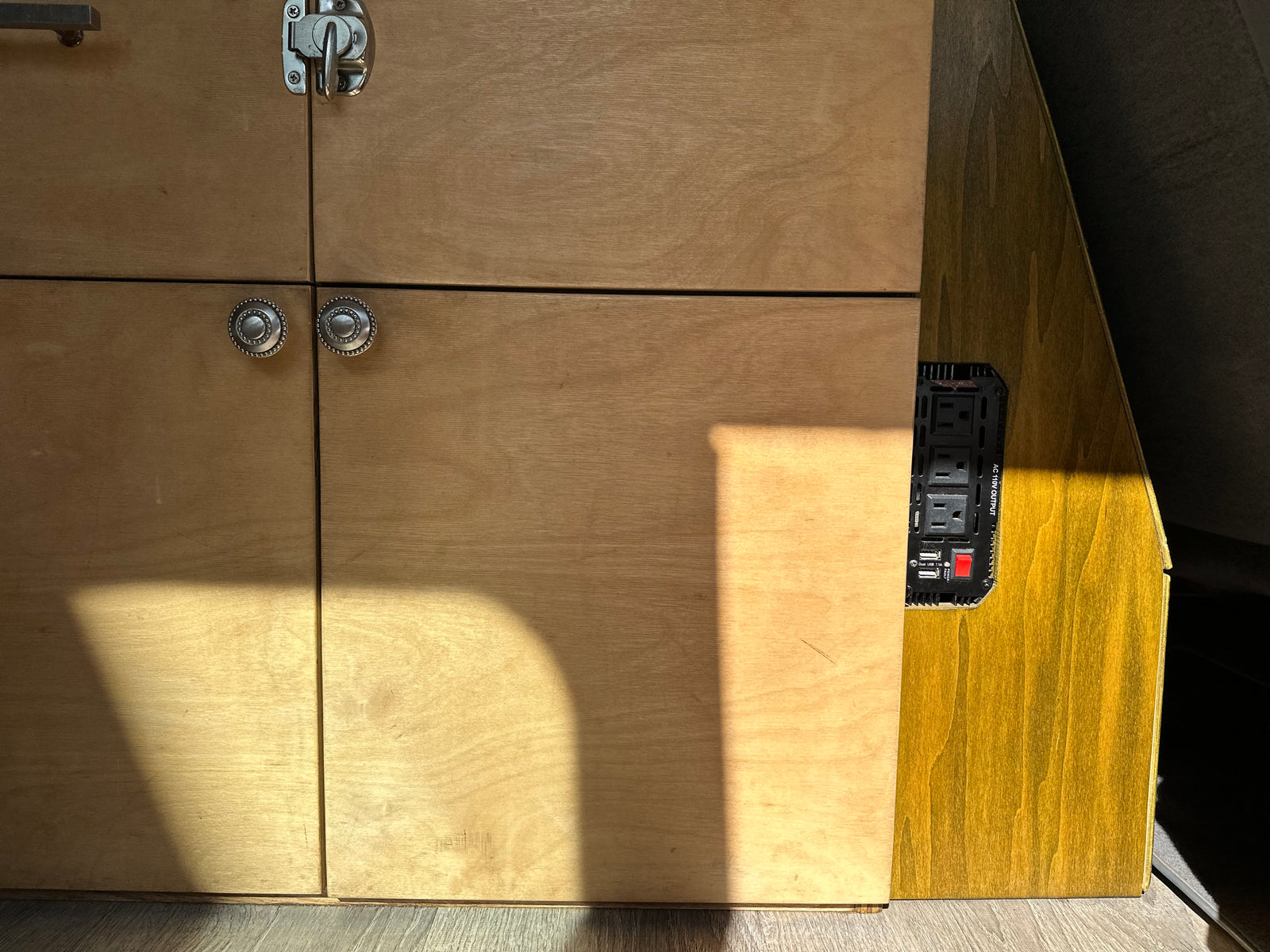 RV rental interior with custom wooden cabinets, power inverter (AC/USB outlets). Sunlight streams in.
