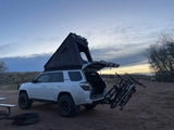 White 4Runner with rooftop tent & bikes at a scenic campsite. Perfect for outdoor adventures, offering more flexibility than an RV rental.
