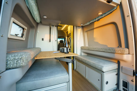 Cozy RV rental interior with dinette seating, adjustable table, and window view for comfortable travel.