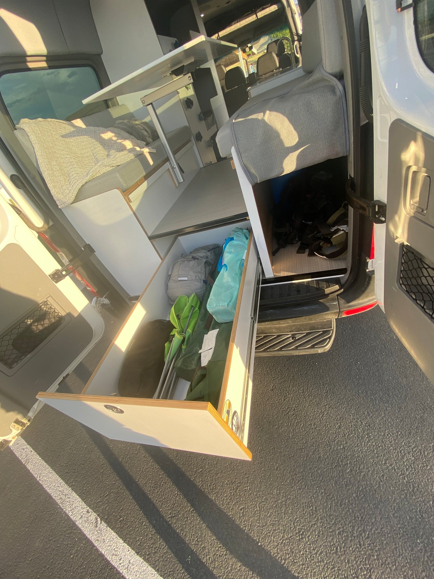 Spacious RV rental interior with a pull-out drawer showing gear, convertible bed, and table setup in a modern camper van.