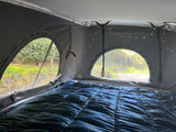 Cozy pop-top RV rental sleeping area with blue bedding, fairy lights, and scenic views. Ideal for camper travel.