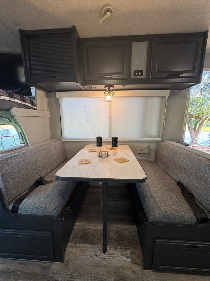 RV rental dinette: grey upholstered benches with seatbelts, a marble-look table, black overhead cabinets, and a scenic window. — photo 8