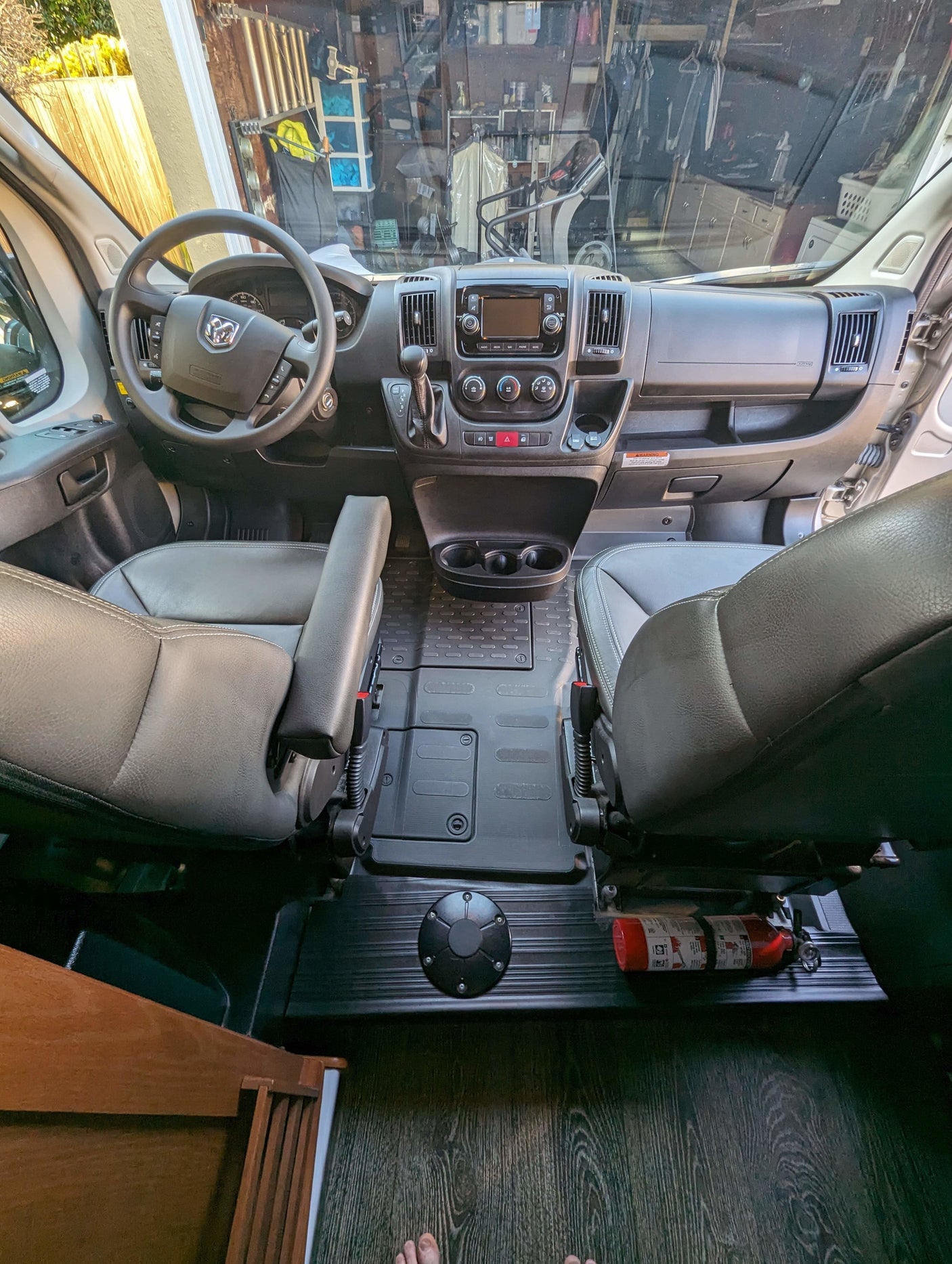 RV rental's front cabin with gray leather swivel seats, dashboard, wood-look floor, and a fire extinguisher.