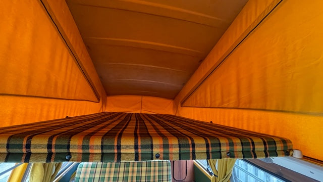 Inside an RV rental pop-top camper: an orange fabric tent above a colorful plaid bunk bed offers cozy sleeping space.