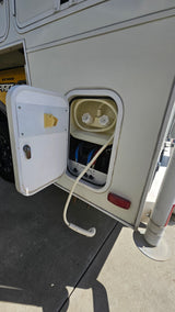 RV rental: Open utility compartment on a white RV, showing an outdoor shower with hose and hot/cold water valves.