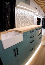 RV rental: Modern kitchen with teal cabinets, wood counters, and a large white farmhouse sink. Bright LED lighting throughout.