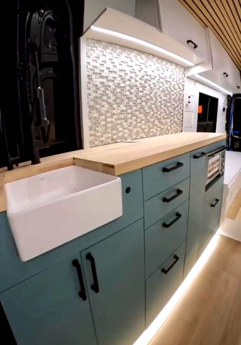  a cozy bed faces open doors revealing a panoramic blue ocean and sky view. Perfect for scenic travel!|RV rental: Modern kitchen with teal cabinets — photo 2
