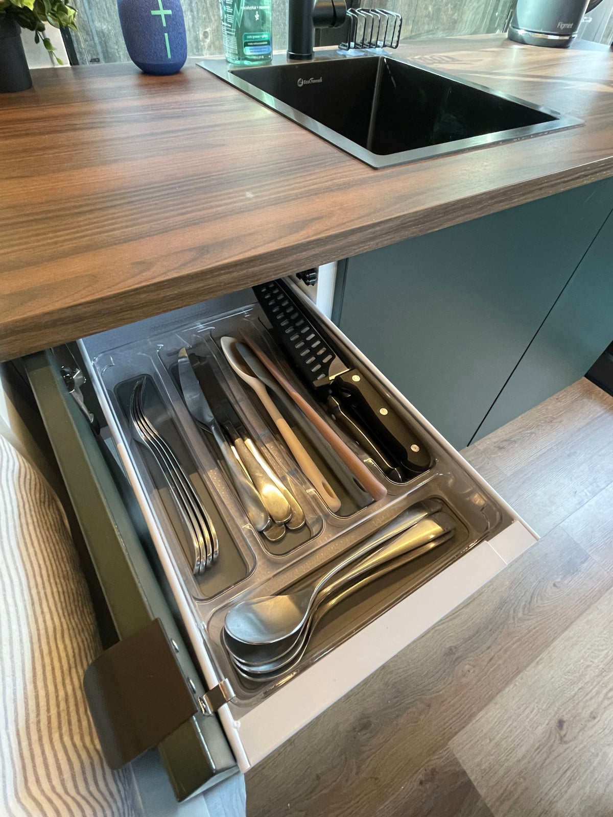 RV rental kitchen: open drawer revealing neatly organized cutlery, knives, and cooking utensils below a wood countertop and sink. — photo 16