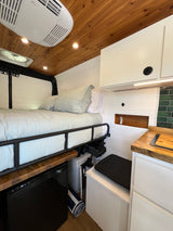RV rental interior: cozy bed, small kitchen with wood counters, refrigerator, water system, and overhead storage.