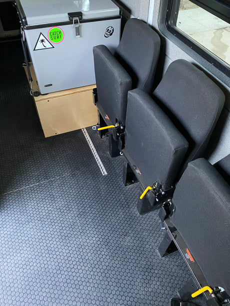 RV rental interior: black modular seats on floor tracks, durable textured floor, and a cooler on a wooden base.