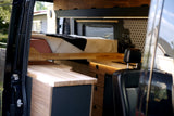 Modern RV rental interior with a cozy bed, wood kitchen, and stylish hexagonal tile backsplash, showcasing custom camper van design.