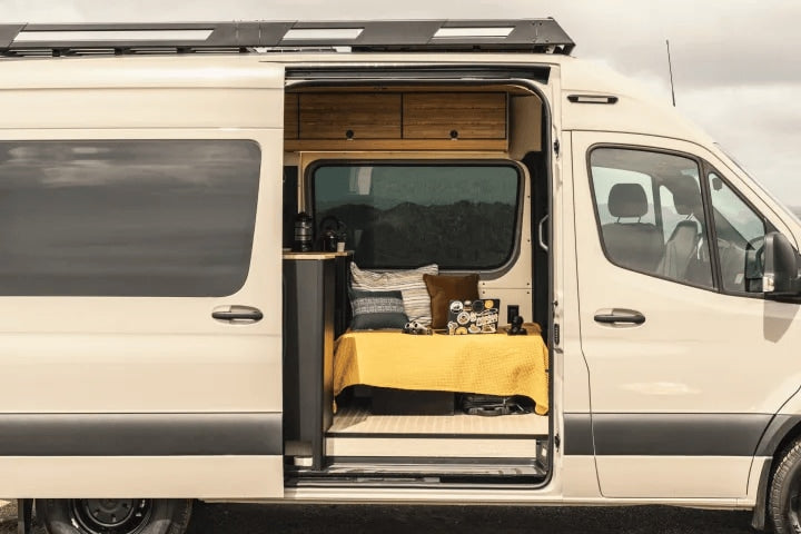 This RV rental shows an open camper van, revealing a cozy interior with a bed, laptop, and small counter. Perfect for travel.