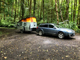 Blue Subaru with pop-top rv rental camper in a lush, mossy forest campsite. Ideal for nature trips.
