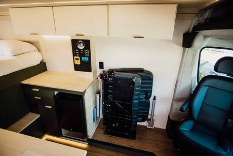This RV rental interior features a cozy bed, counter with fridge, control panel, and folded passenger seats, maximizing space.