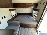 Cozy RV rental interior featuring a comfortable bed, dinette with table, and overhead storage cabinets for travel.