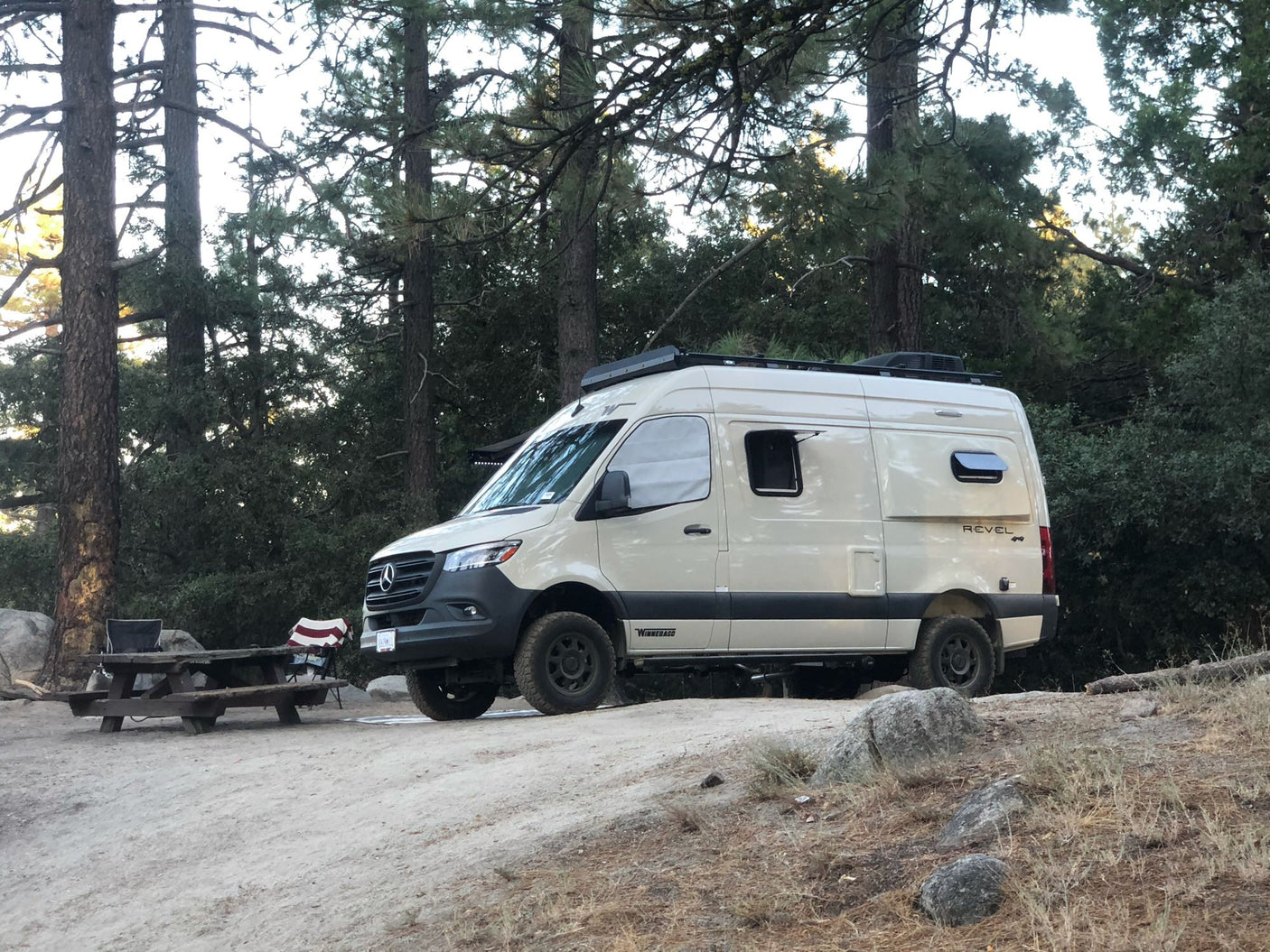 Beige Winnebago Revel Sprinter RV rental parked at a rustic campsite with a picnic table, ready for adventure.