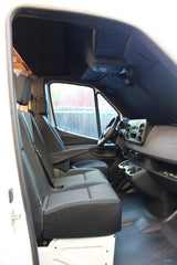 Inside an RV rental van's front cabin, showing driver & passenger seats, steering wheel, and dashboard. Ready for adventure!