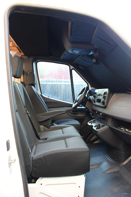 Inside an RV rental van's front cabin, showing driver & passenger seats, steering wheel, and dashboard. Ready for adventure!