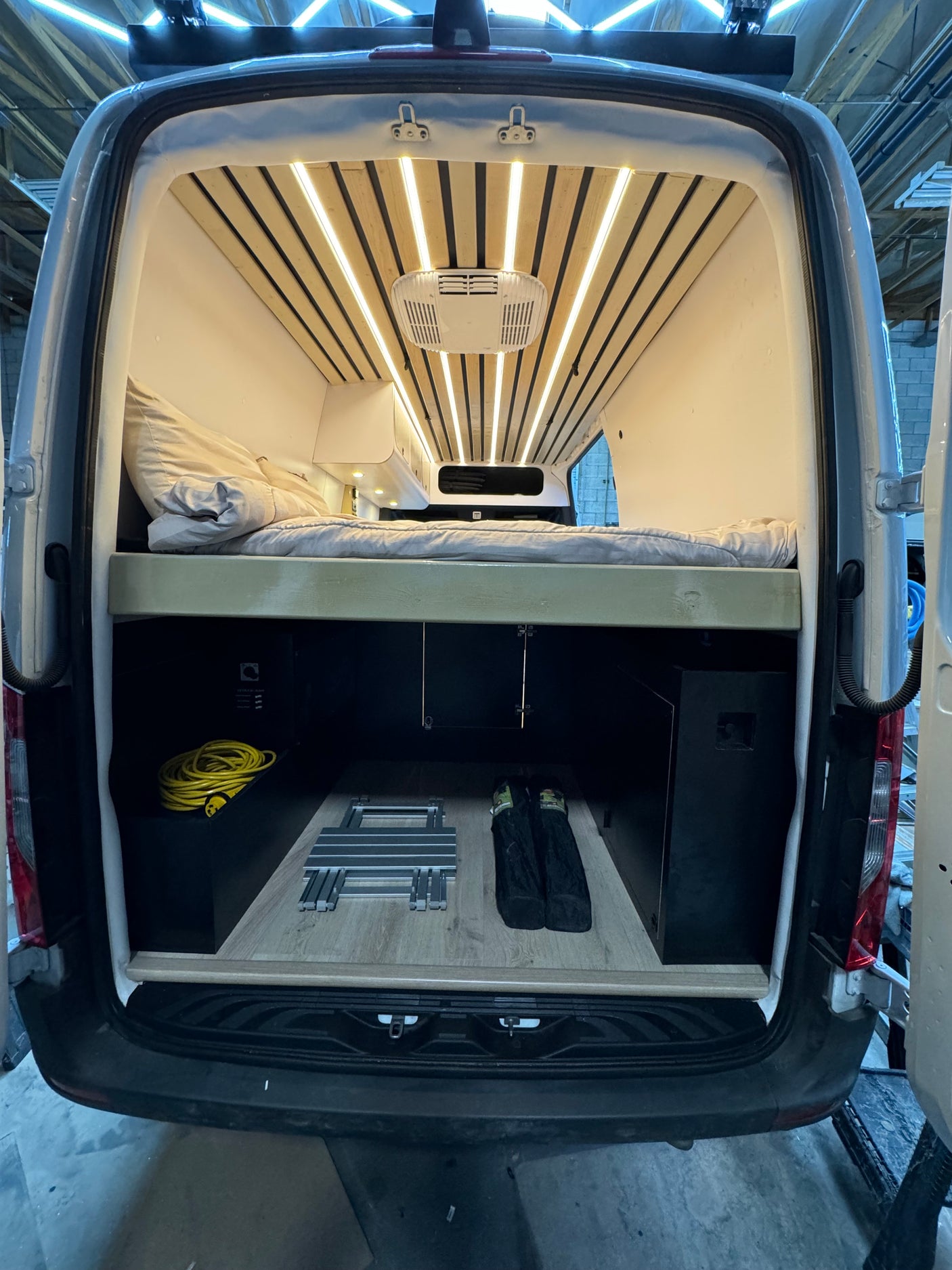 Rear view of a custom camper van interior, ideal for rv rental, featuring a bed, under-bed storage, and LED ceiling lights.