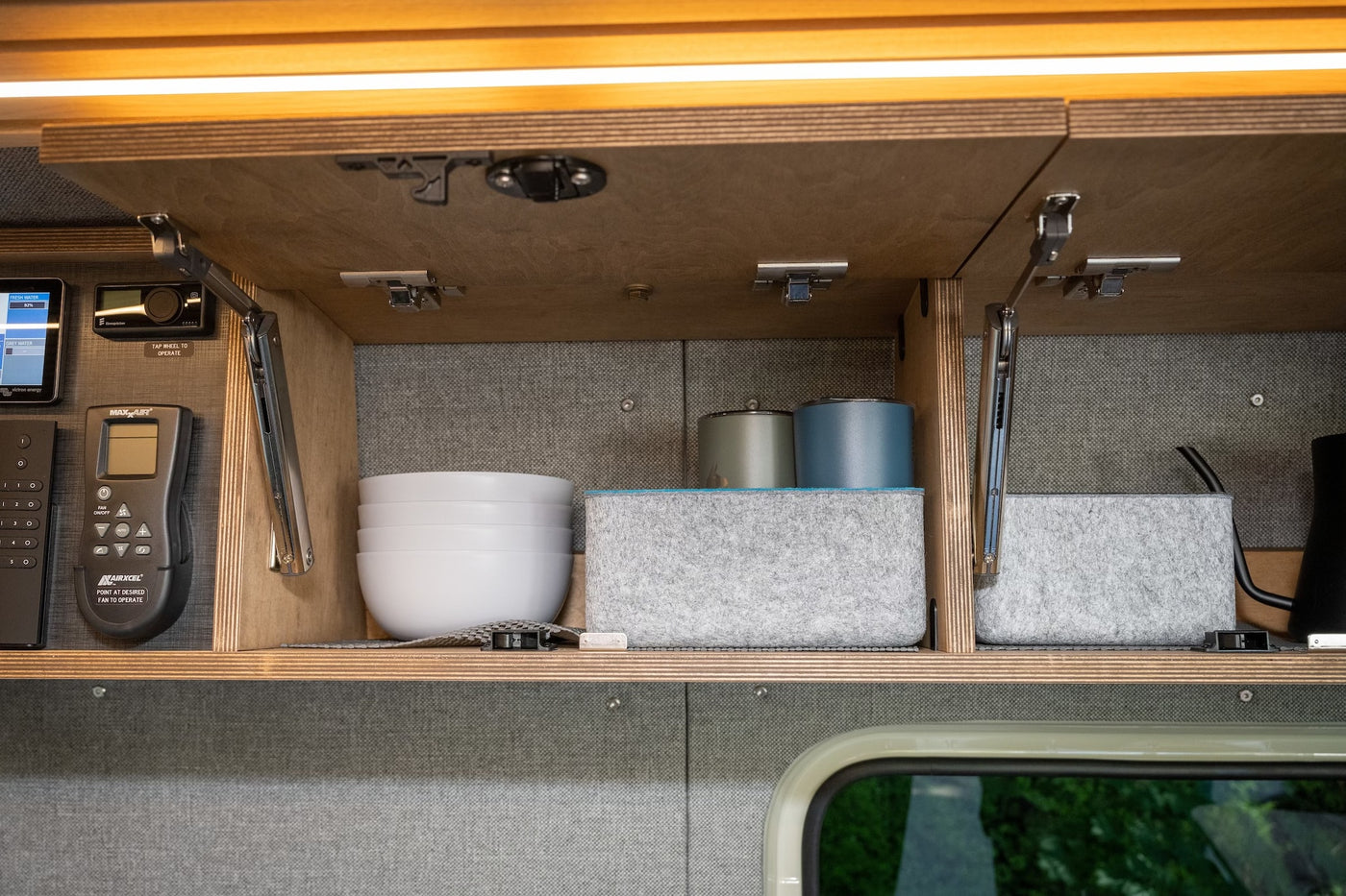Inside an RV rental overhead cabinet: smart controls for water, heat, and fan, plus neatly stored kitchenware. — photo 13