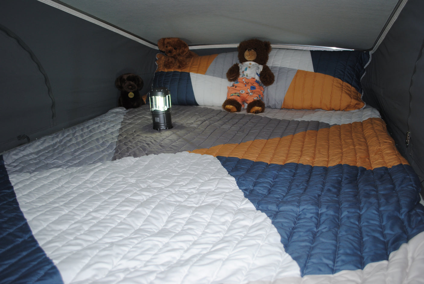Inviting RV rental camper bed with geometric quilt, fluffy teddy bears, and lit lantern for cozy adventures.