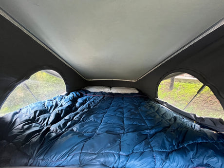 Cozy sleeping area inside an rv rental, featuring a blue comforter, pillows, and pop-top windows to nature.