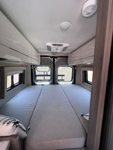 Spacious RV rental interior featuring a large bed, overhead storage, AC unit, and rear windows, ready for travel.