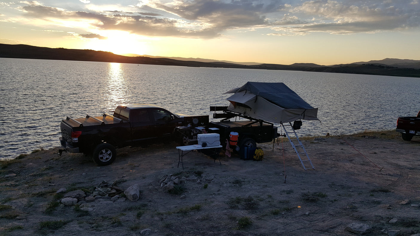 Sunset at a lake campsite. Truck with an overlanding trailer & rooftop tent offers an amazing outdoor RV rental experience.
