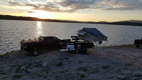 Sunset at a lake campsite. Truck with an overlanding trailer & rooftop tent offers an amazing outdoor RV rental experience.