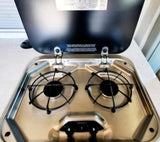 Stainless steel two-burner gas stove with black grates inside an RV rental. A compact kitchen essential for your travels.