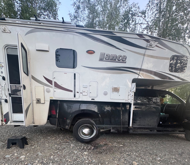 This white Lance truck camper, a type of RV rental, is ready for adventure. Open door & outdoor step visible.