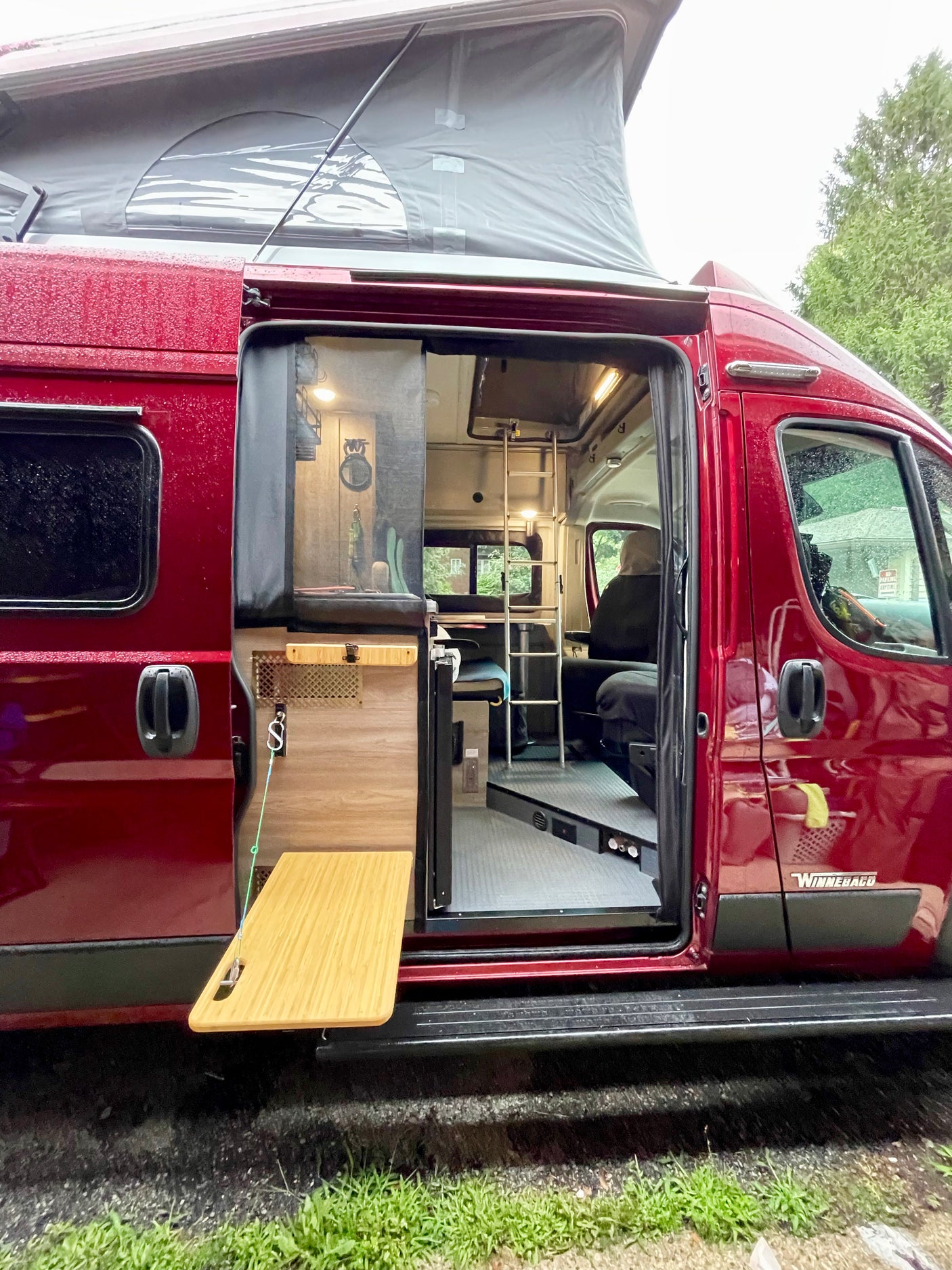 Red Winnebago camper van RV rental with pop-top roof extended and interior visible through open side door.