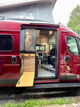 Red Winnebago camper van RV rental with pop-top roof extended and interior visible through open side door.