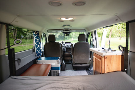 View from the rear of an RV rental: a compact interior with bed, Dometic cooler, sink, and driver's cab.