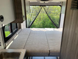 Cozy RV rental interior with a comfortable bed, rear screened window, and nature view.