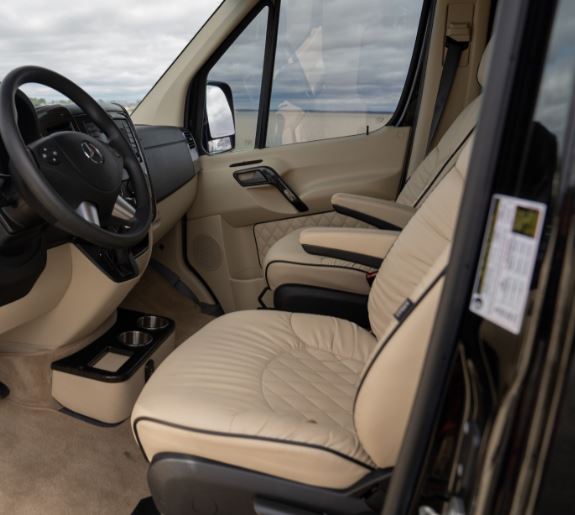  showing the compact bathroom with a toilet and a small kitchen area with a microwave.|Inside a luxury RV rental: cream quilted seats