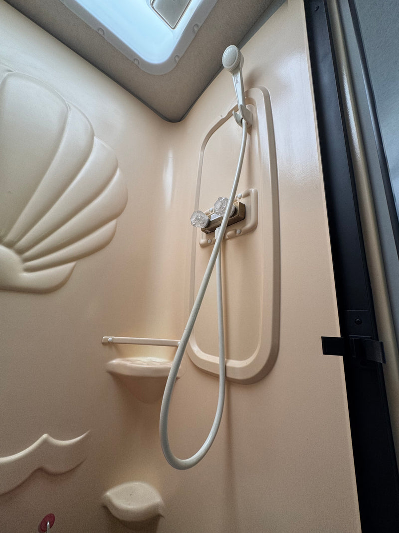 Beige, compact shower in an rv rental, featuring a shell design, handheld shower, and overhead skylight. — photo 13