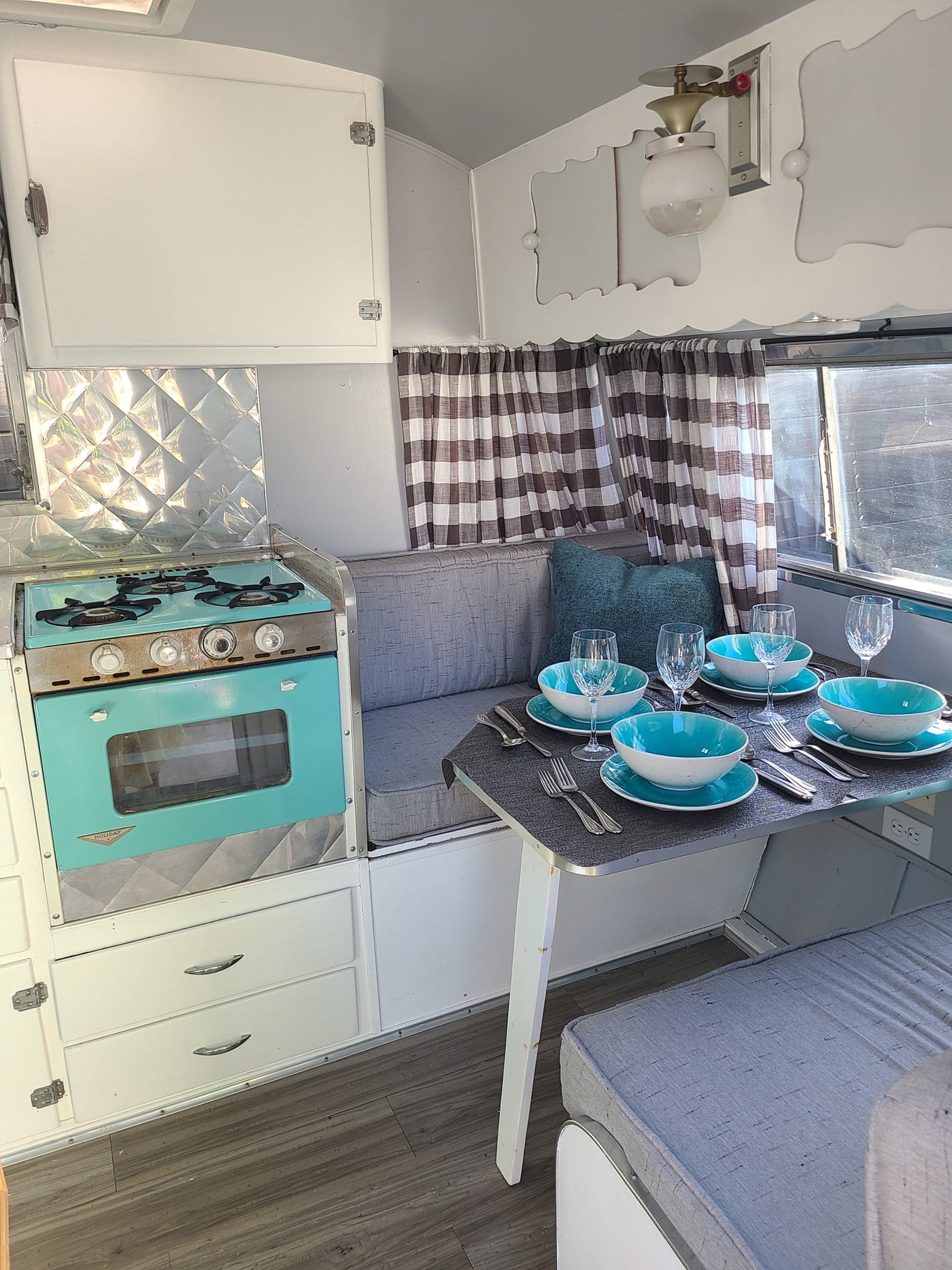 Cozy vintage RV rental interior featuring a turquoise stove, dining set with blue bowls, and plaid curtains. — photo 11