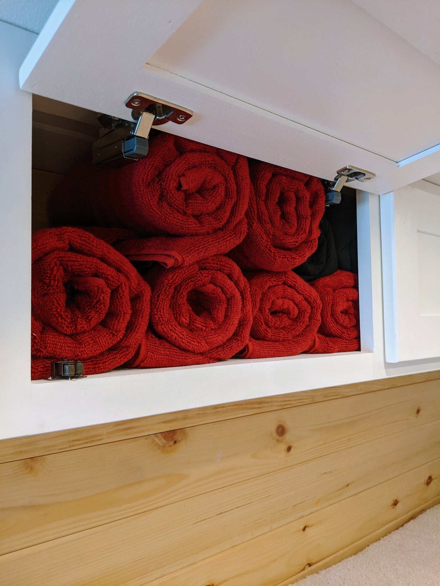 RV rental storage: Neatly rolled red towels in an open overhead cabinet with wood paneling below.