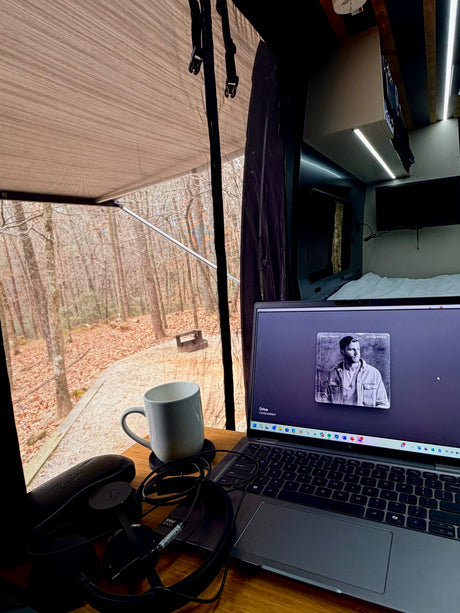 An RV rental offers a perfect mobile workspace: laptop, coffee, headphones, and a tranquil forest view through the screen.