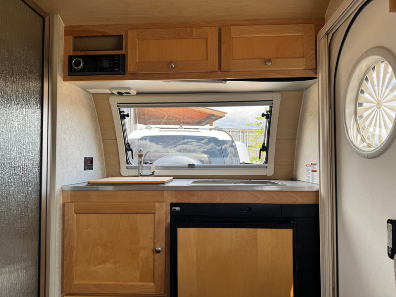 This RV rental's compact kitchen boasts wood cabinets, a sink, small fridge, stereo, and a window view. — photo 13