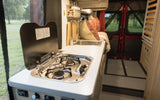 Enjoy an RV rental's compact kitchen with a stove and sink, overlooking nature through a screened window.