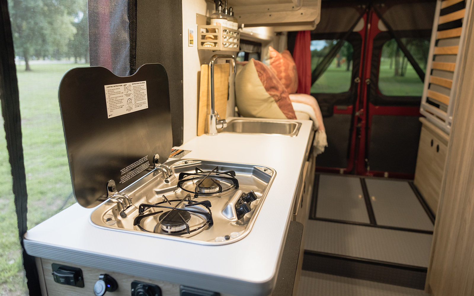 Enjoy an RV rental's compact kitchen with a stove and sink, overlooking nature through a screened window.