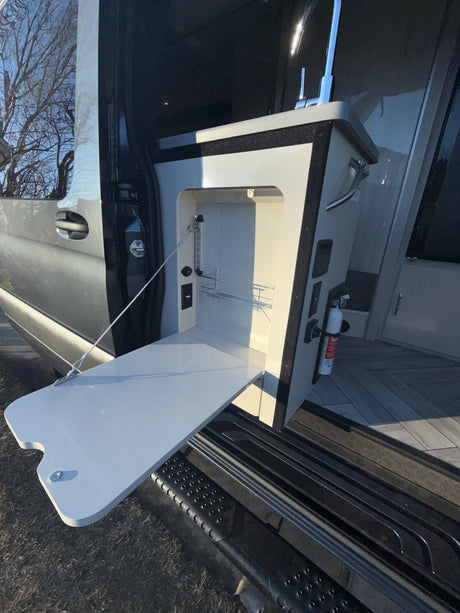 RV rental kitchen setup with pull-out table, sink, and fire extinguisher for outdoor use.
