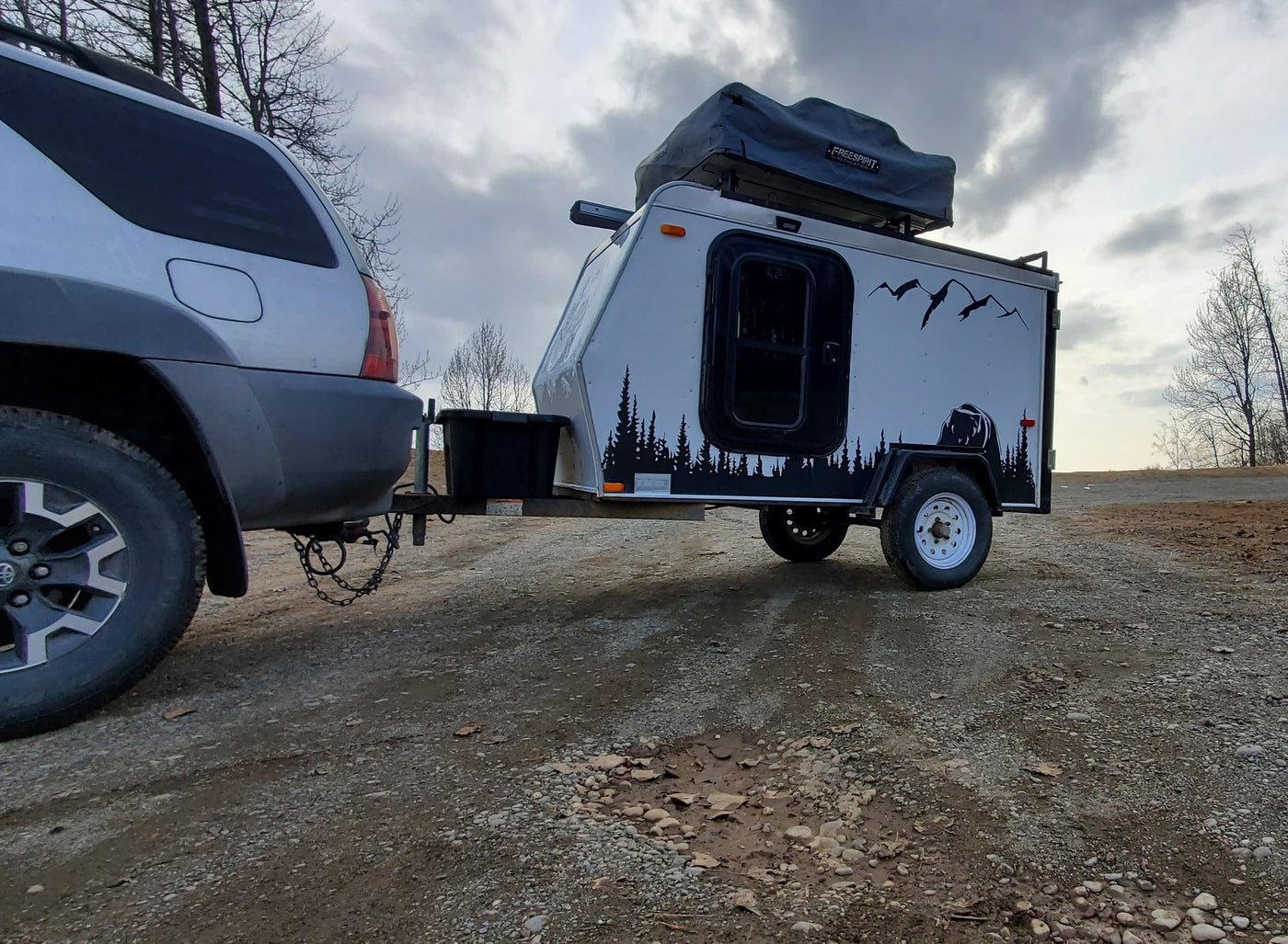 An SUV tows an RV rental teardrop camper with a rooftop tent, ready for outdoor travel on a dirt road. — photo 2