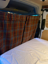 Cozy RV rental interior: a bed with white sheets and warm plaid privacy curtains.