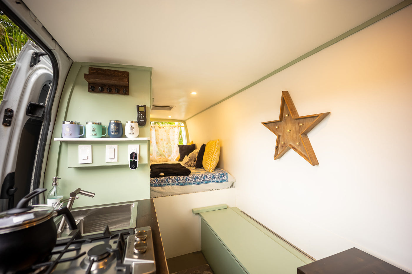 Inside a stylish RV rental: a compact kitchen, comfy bed area, and storage, all in light green & white. — photo 2