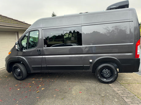 Sleek gray camper van, ideal for RV rental. Side view with windows, roof AC unit, and external electrical connection.